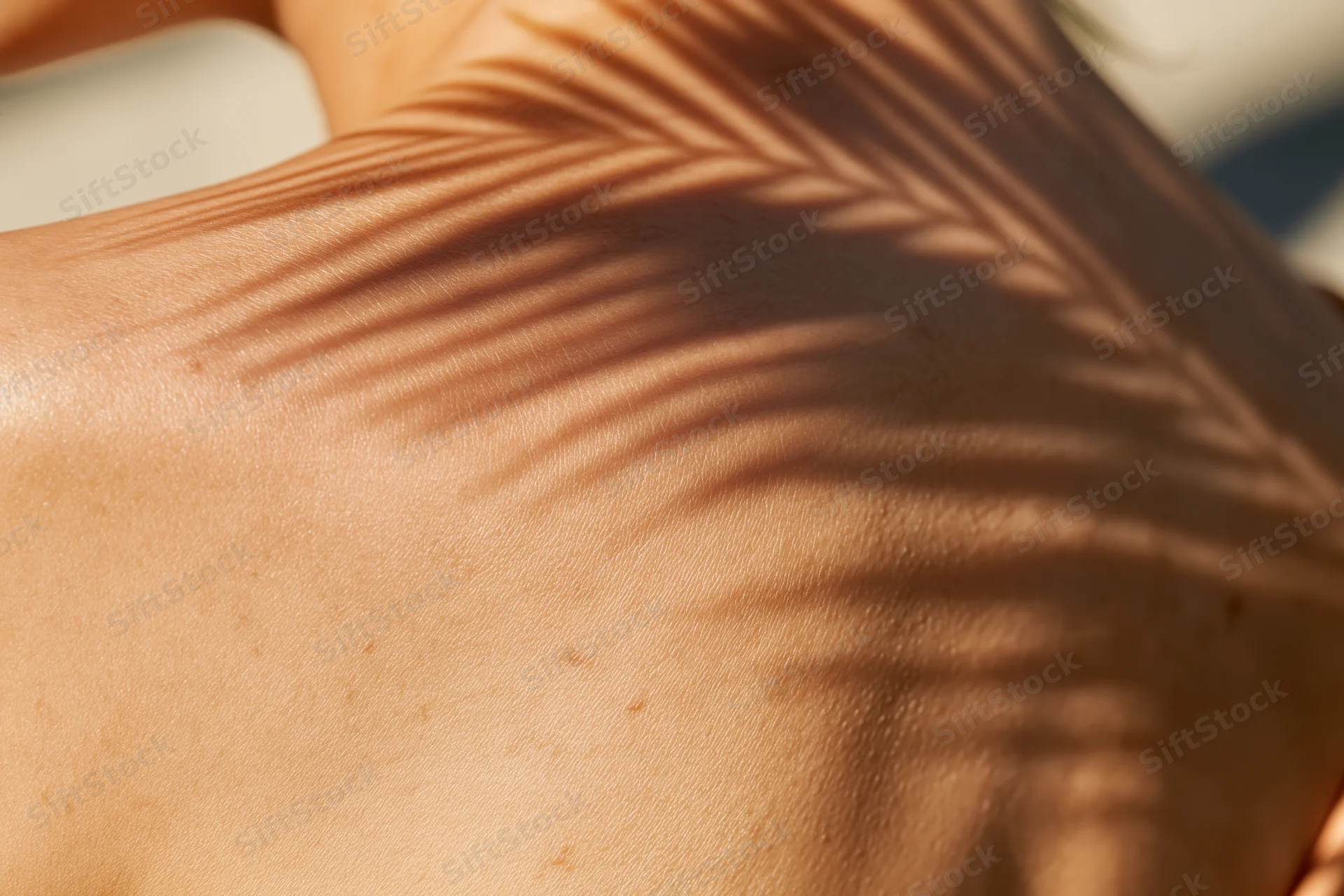 Close-up of a woman's bare shoulder and back with palm leaf shadows in warm sunlight