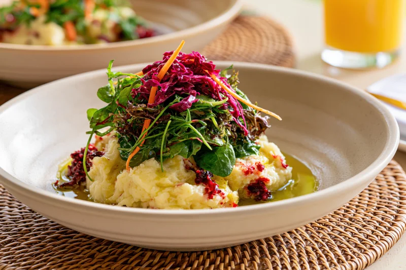 Creamy mashed potatoes topped with mixed greens and shredded beets in a ceramic bowl on a woven placemat