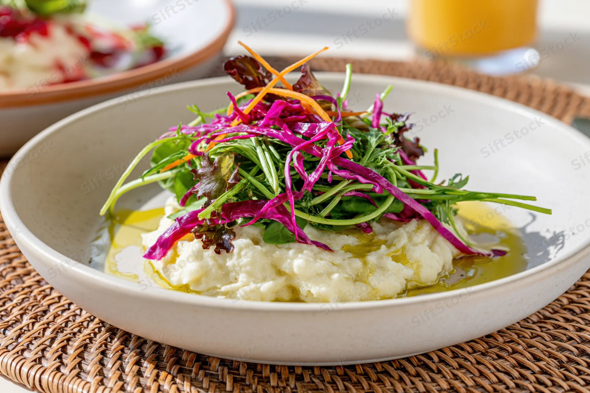 Close-up of a salad with mashed cauliflower and olive oil in a white bowl on a woven placemat