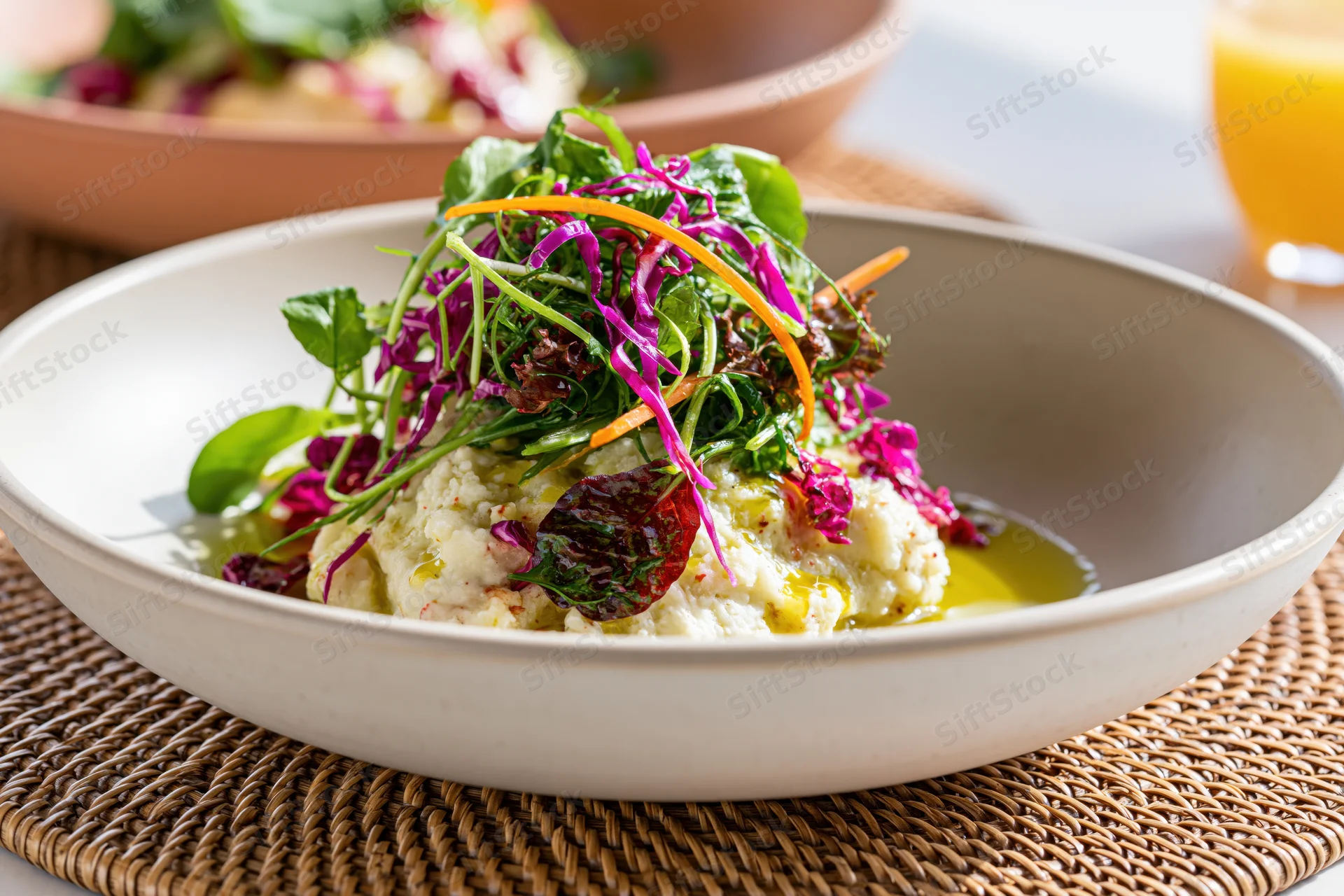 Creamy mashed cauliflower topped with mixed greens and vegetable slivers in a white bowl on a woven placemat