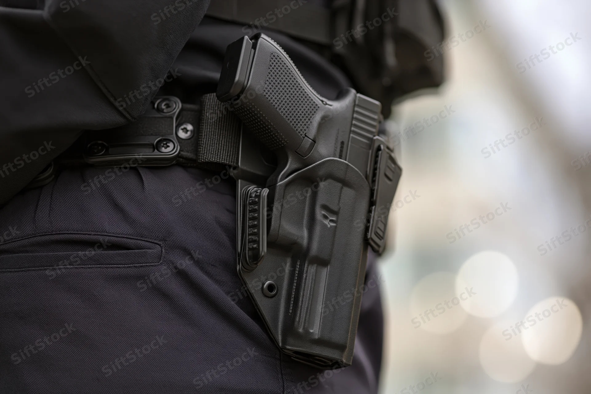 Close-up of a black handgun in a tactical duty holster worn on a police officer's belt