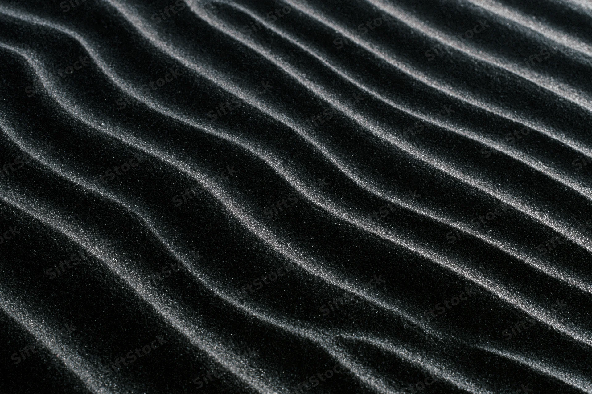 Rippled black volcanic sand dunes forming wavy patterns across the desert surface
