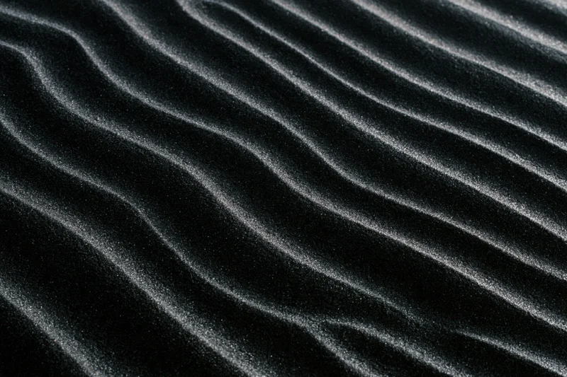 Rippled black volcanic sand dunes forming wavy patterns across the desert surface