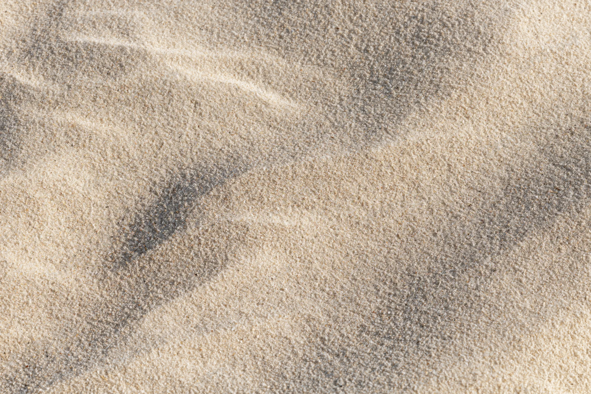 Close-up overhead view of smooth dry beach sand with natural ripples and shadows