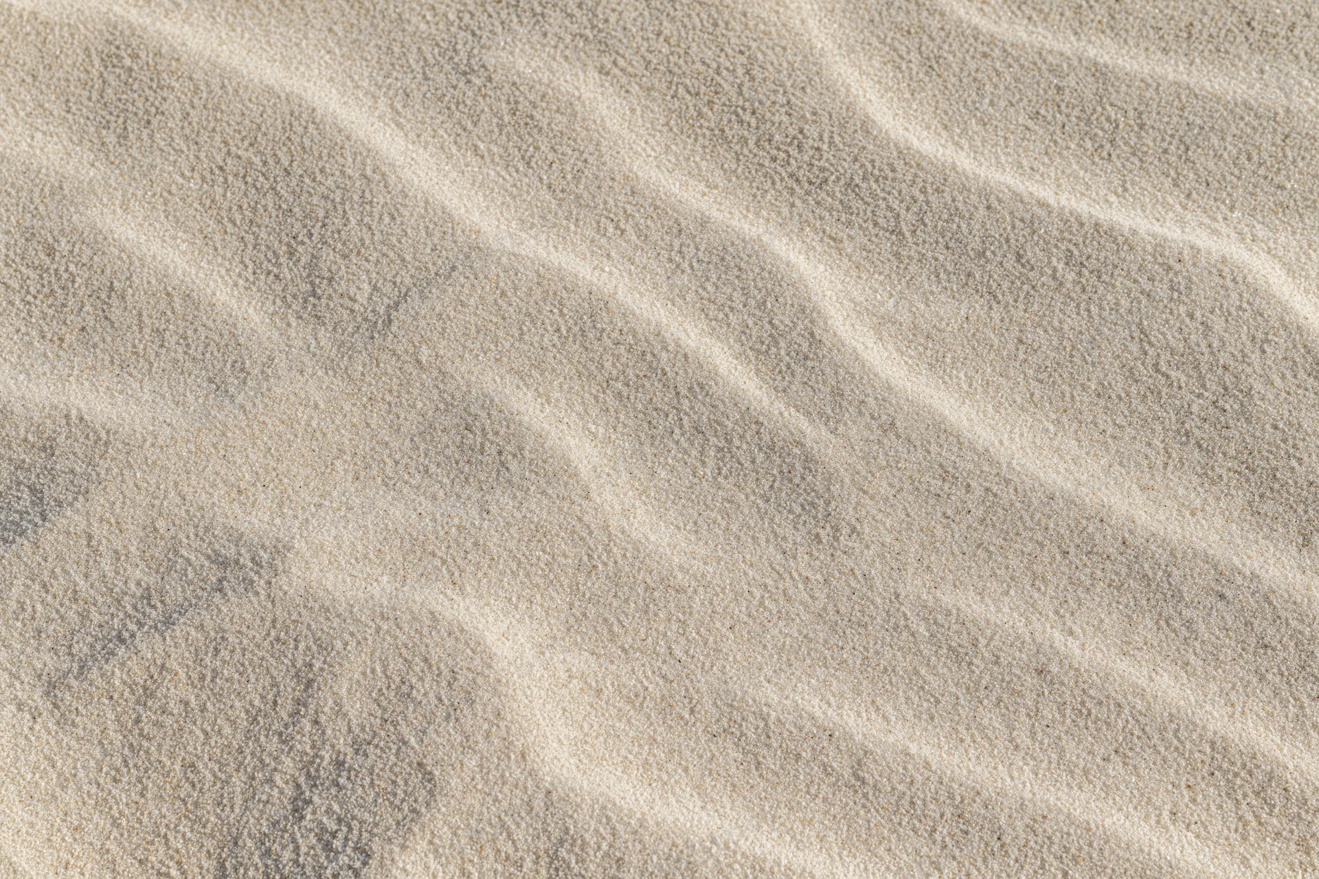 Close-up overhead view of smooth dry beach sand with rippled texture filling the frame