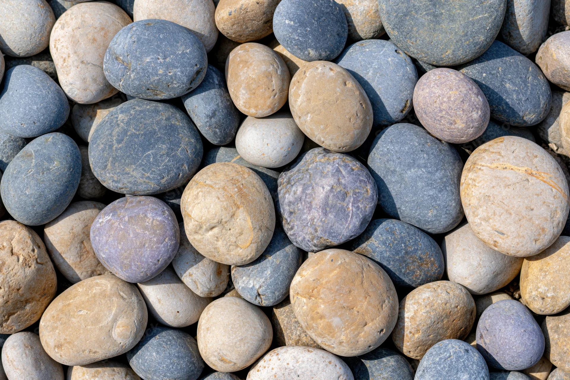 Close-up overhead view of smooth rounded river pebbles in natural colors scattered on a flat surface