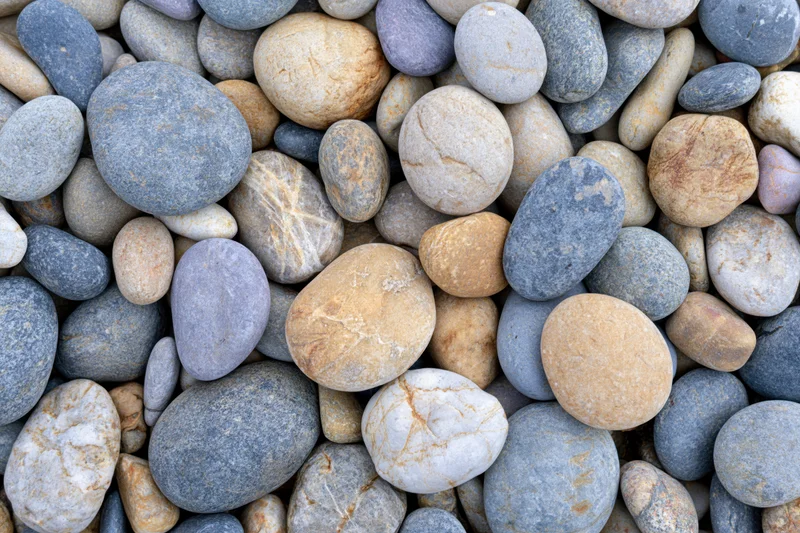 Close-up overhead view of smooth rounded river pebbles in natural colors scattered densely across the frame