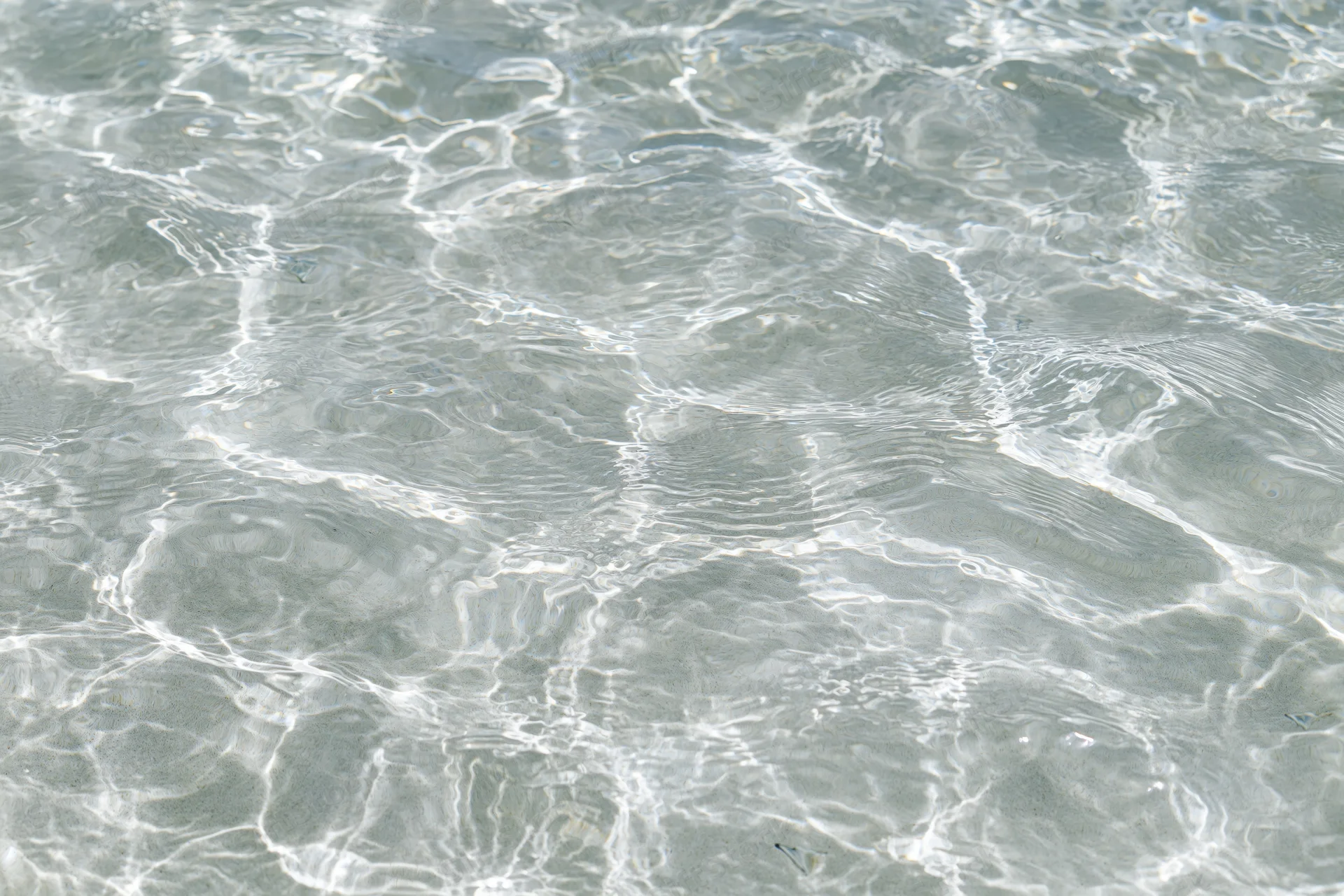 Clear shallow water surface with ripples and light reflections over sand