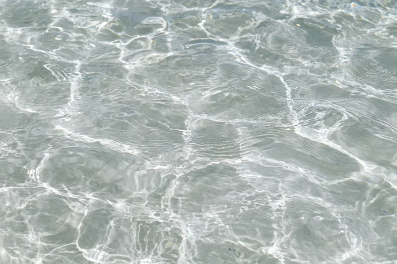 Clear shallow water surface with ripples and light reflections over sand