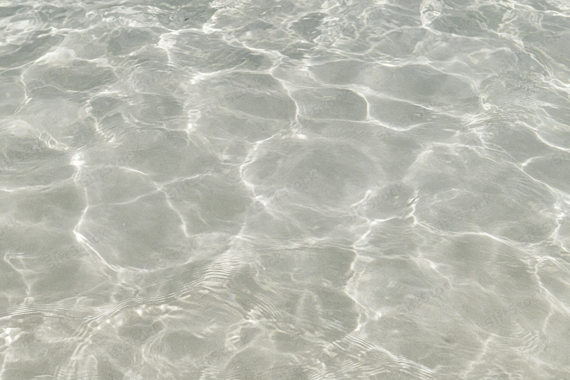 Clear shallow water surface with ripples and light reflections over sand