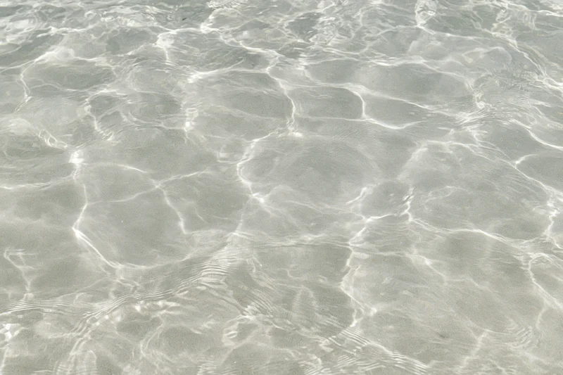 Clear shallow water surface with ripples and light reflections over sand