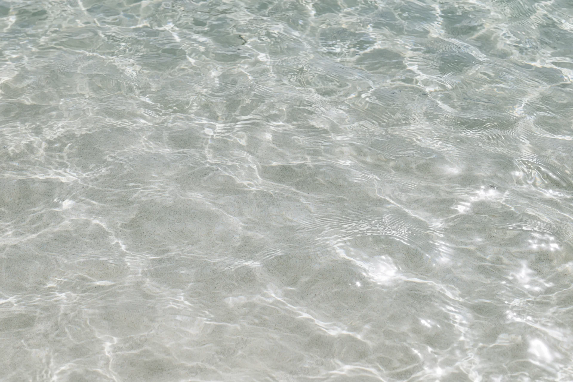 Clear shallow water surface with ripples and light reflections over sandy seabed
