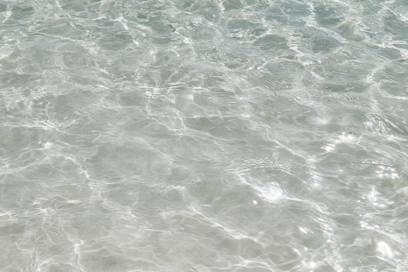 Clear shallow water surface with ripples and light reflections over sandy seabed