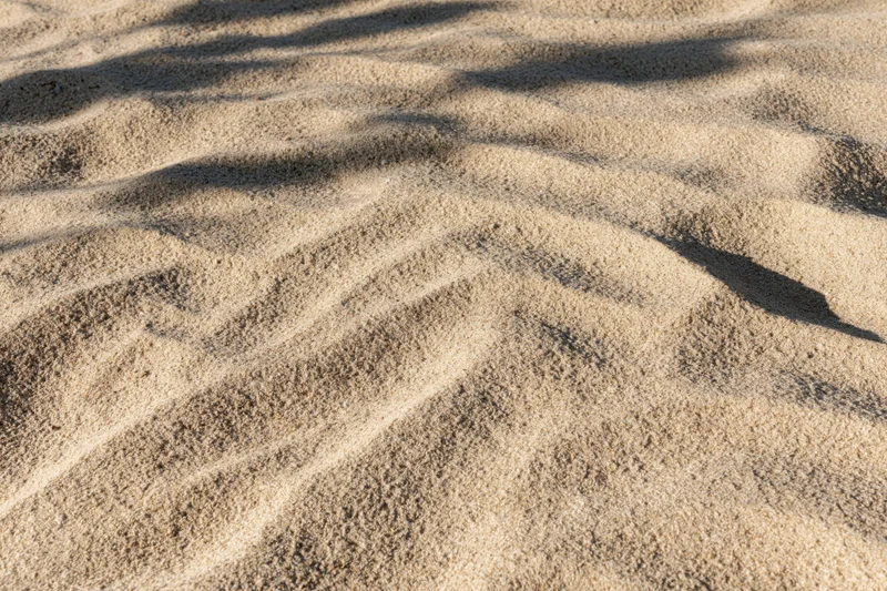 Closeup of rippled dry beach sand surface under sunlight