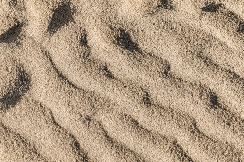 Close-up overhead view of dry beach sand surface with natural ripples and grain texture