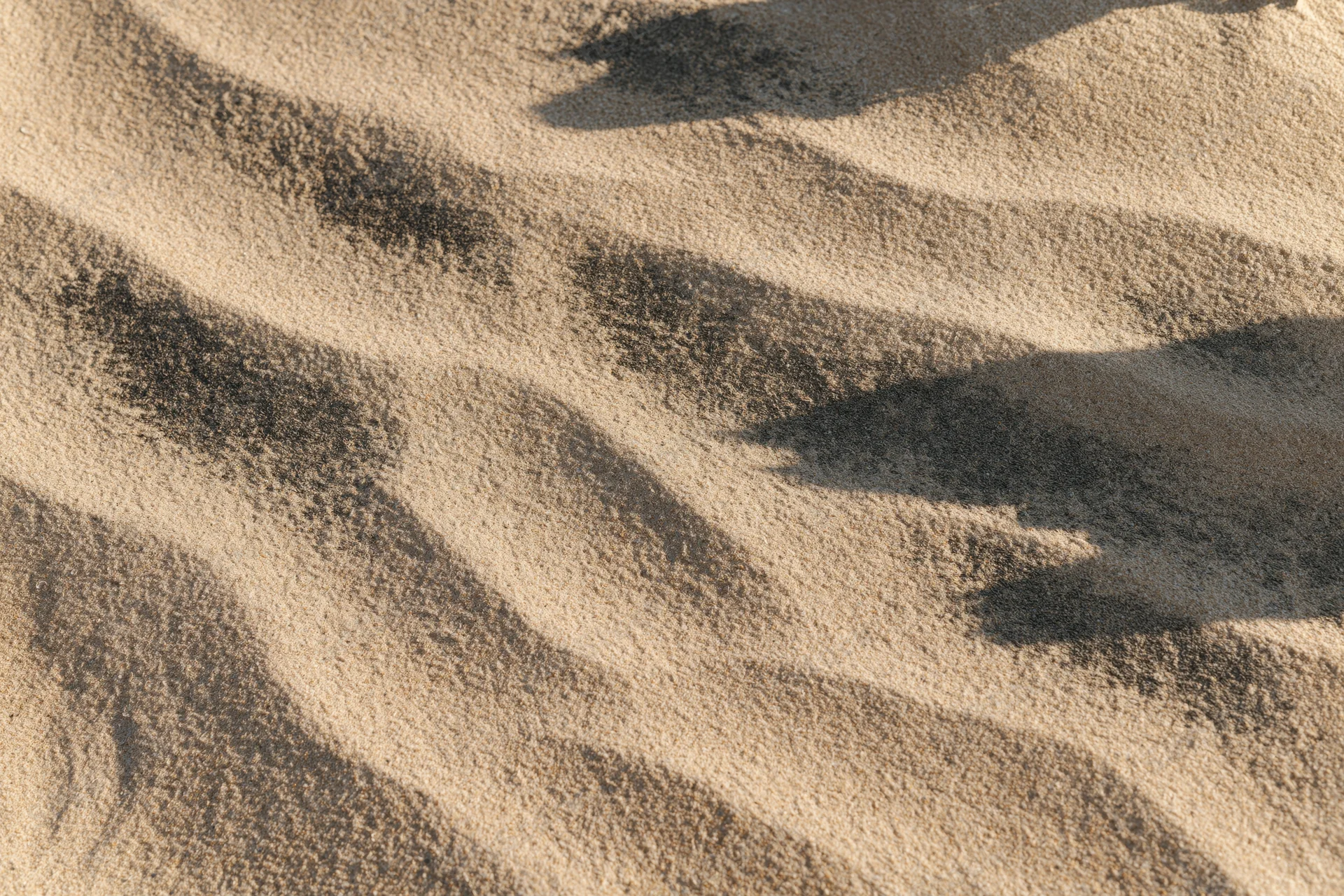 Closeup overhead view of dry beach sand with rippled texture and shadows from sunlight