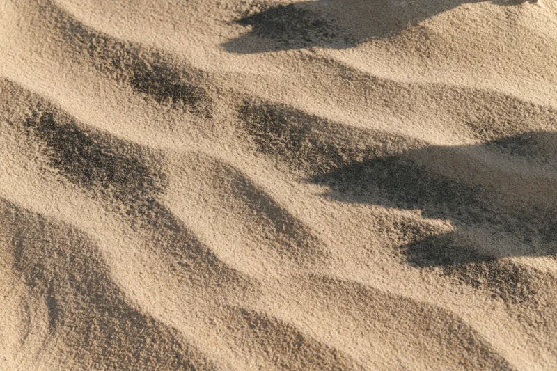 Closeup overhead view of dry beach sand with rippled texture and shadows from sunlight