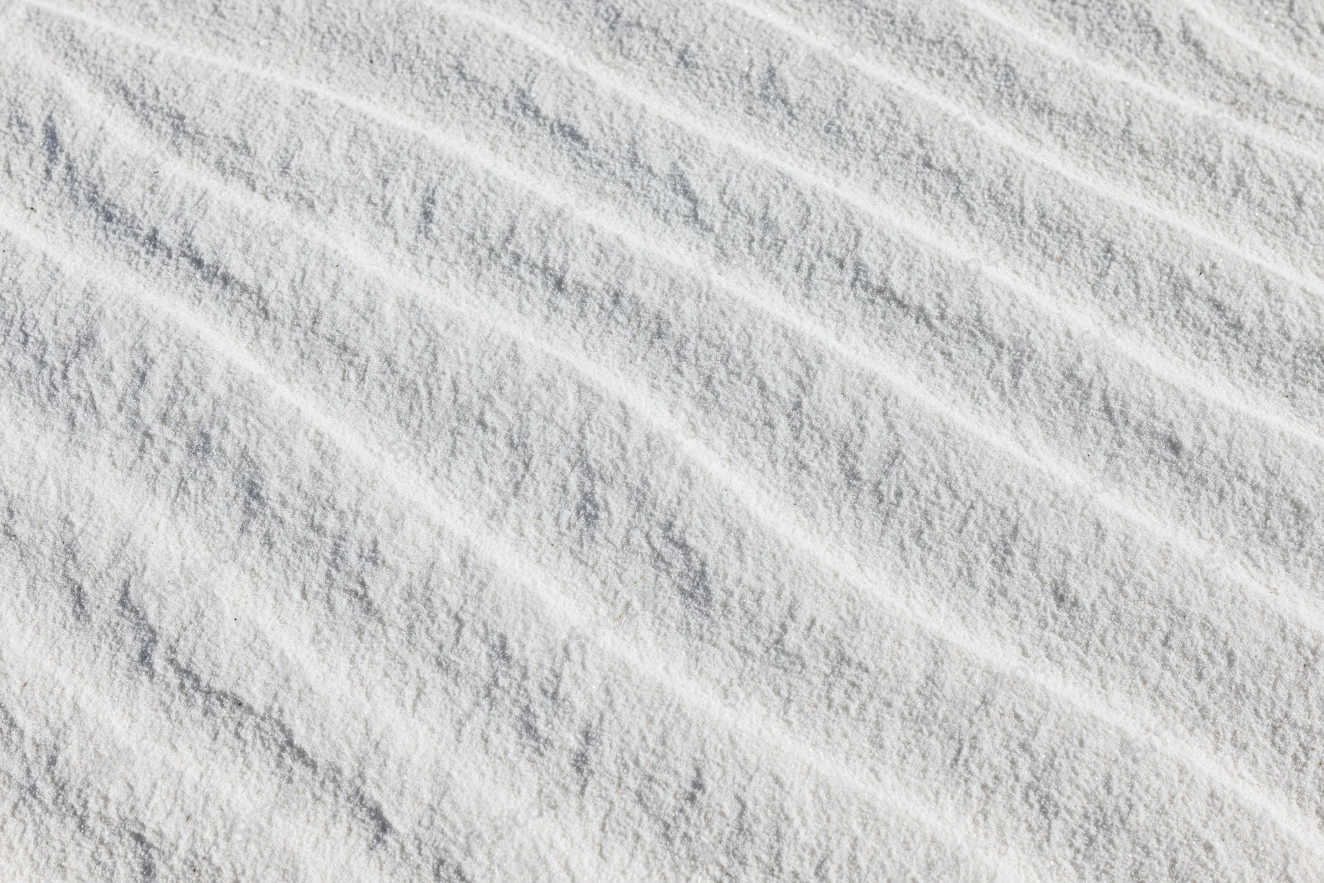 Close-up overhead view of white sand with wind-formed ripples across the surface