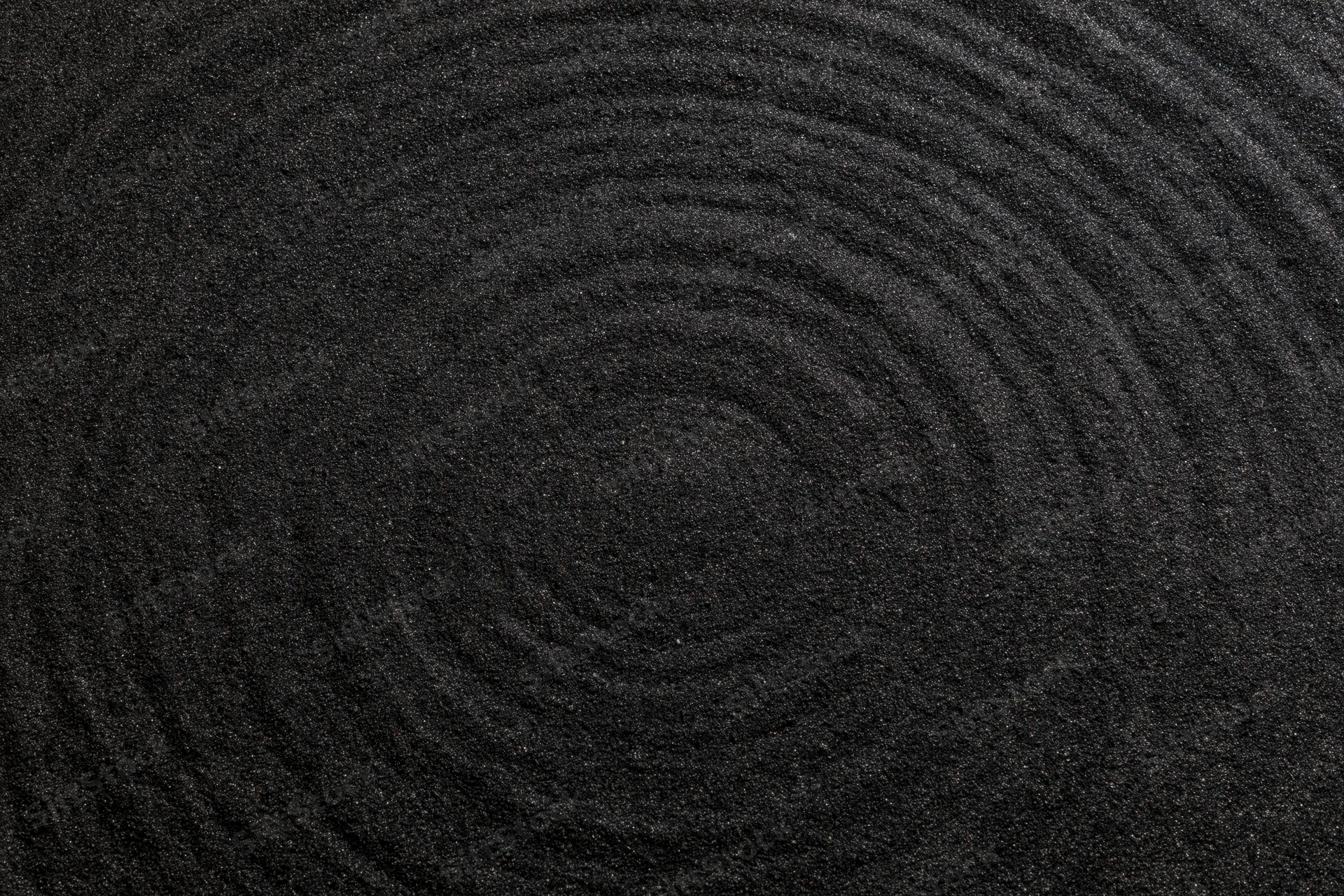 Concentric circles raked into dark black volcanic sand surface