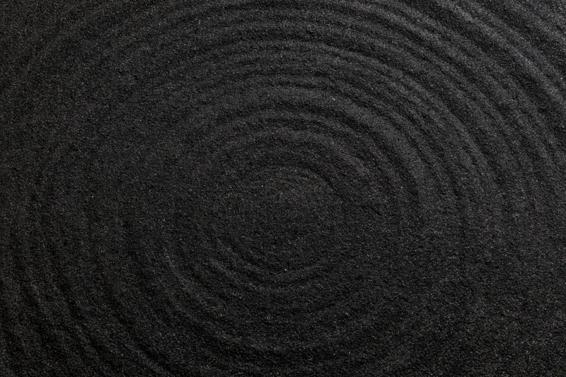 Concentric circles raked into dark black volcanic sand surface