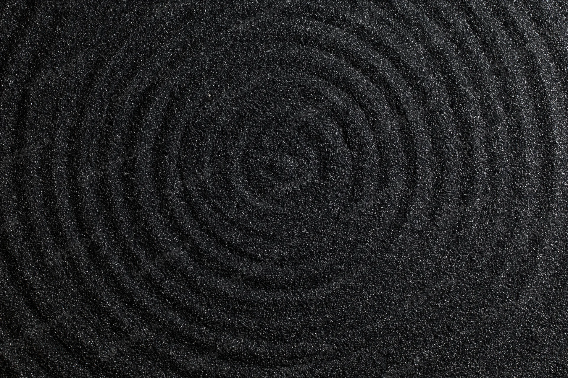 Concentric circles raked into dark black volcanic sand surface