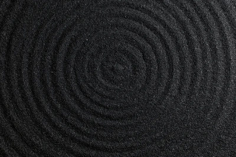 Concentric circles raked into dark black volcanic sand surface