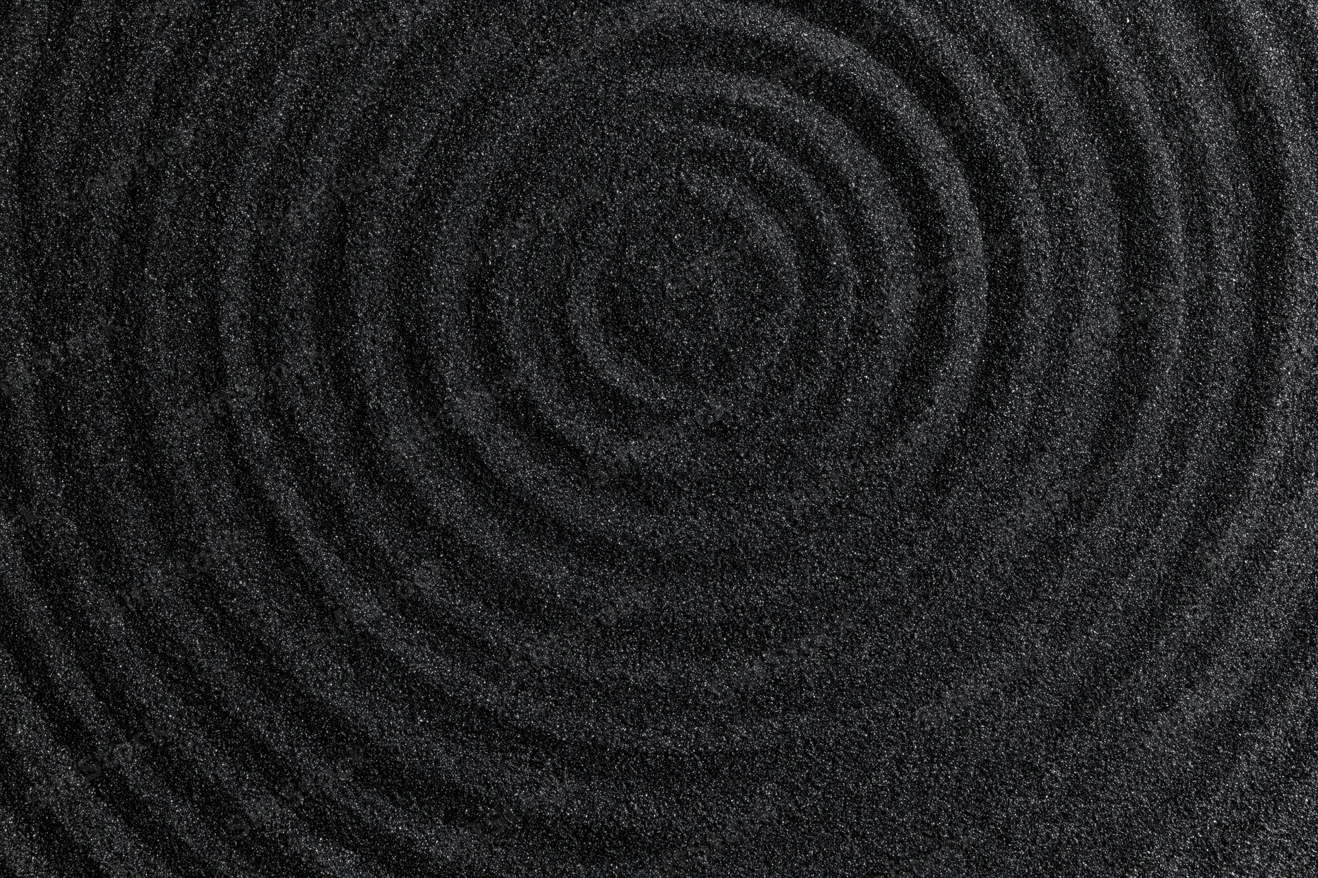Concentric circles raked into dark volcanic sand forming a spiral pattern
