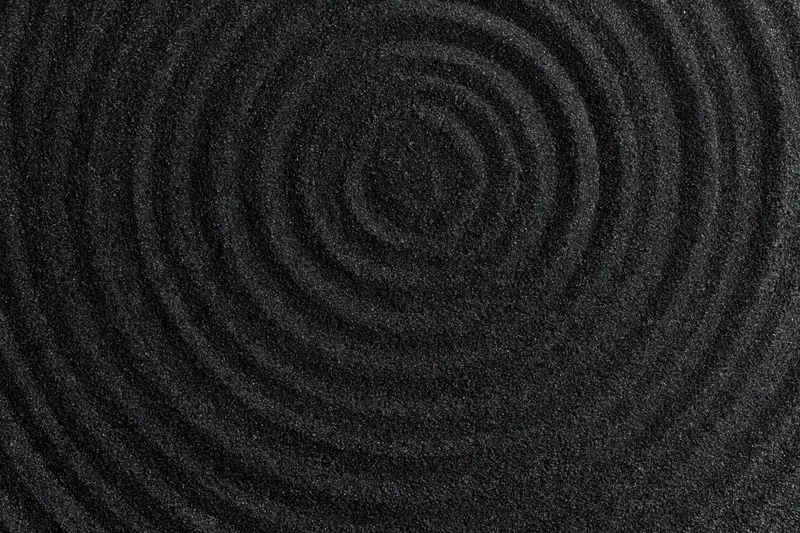 Concentric circles raked into dark volcanic sand forming a spiral pattern