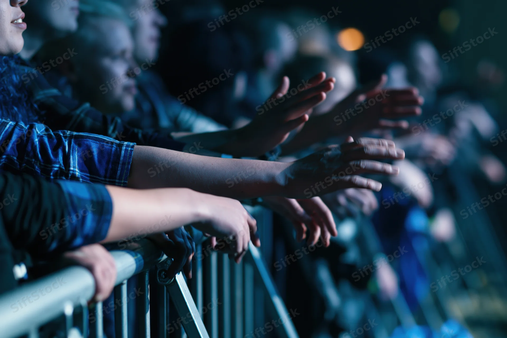 Concert crowd leaning over metal barrier with arms and hands extended toward stage