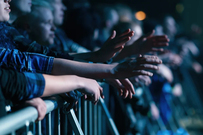 Concert crowd leaning over metal barrier with arms and hands extended toward stage