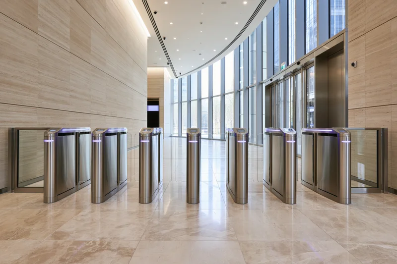 Row of stainless steel turnstiles in a modern corporate office lobby with glass walls and marble flooring