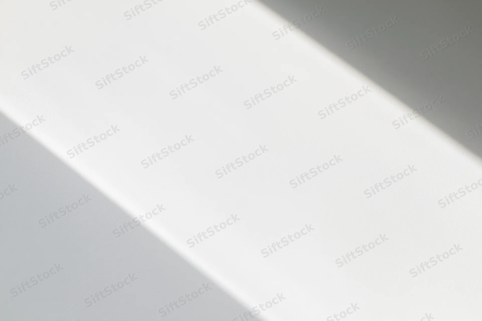 Diagonal band of natural light across a plain white surface