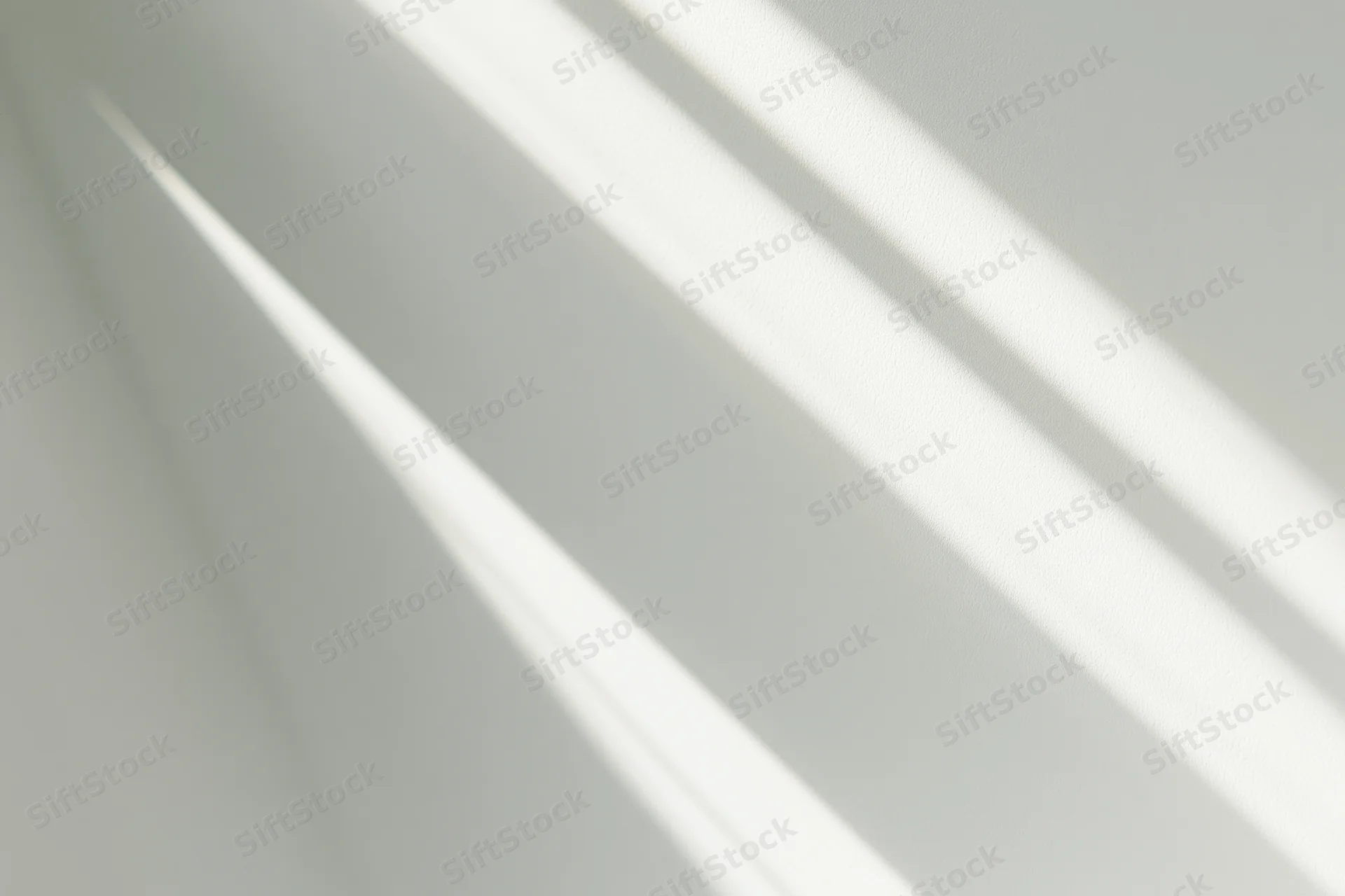 Diagonal bands of natural sunlight and soft shadow on a white wall indoors