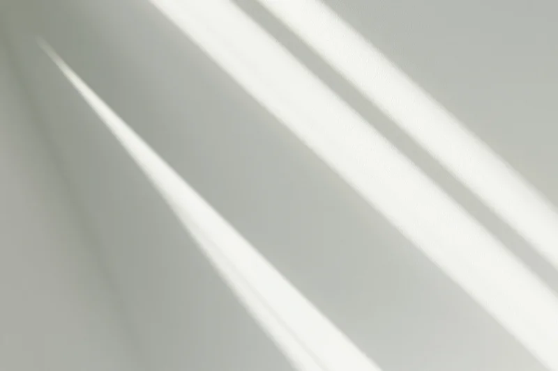 Diagonal bands of natural sunlight and soft shadow on a white wall indoors