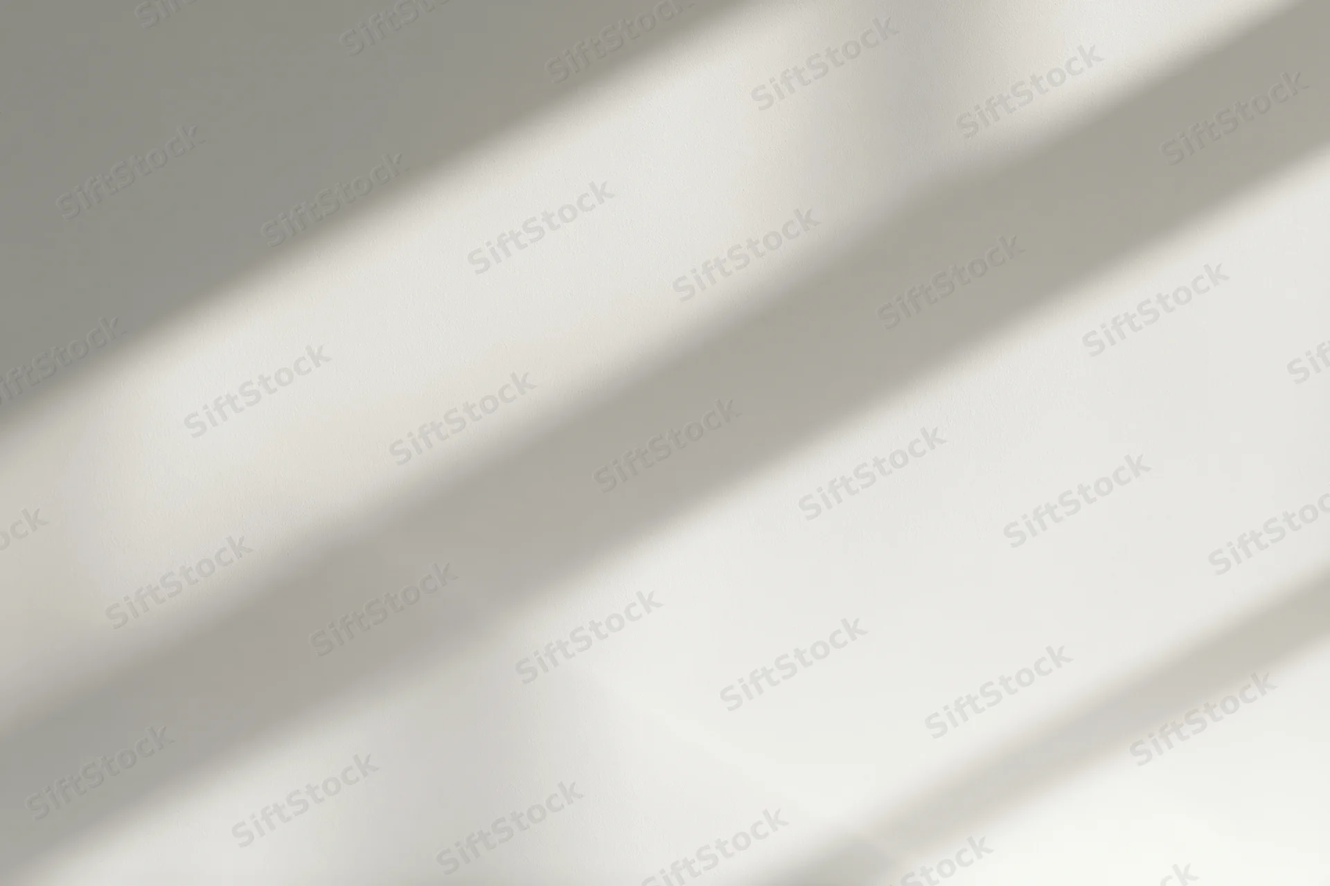 Diagonal bands of natural window light and soft shadow falling across a plain indoor surface