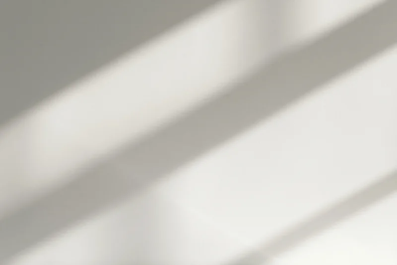 Diagonal bands of natural window light and soft shadow falling across a plain indoor surface
