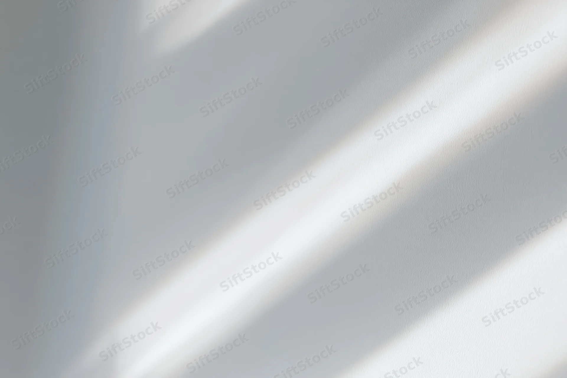 Diagonal bands of natural sunlight and soft shadow on a white interior wall