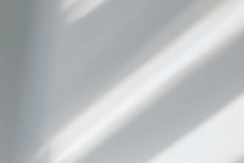 Diagonal bands of natural sunlight and soft shadow on a white interior wall