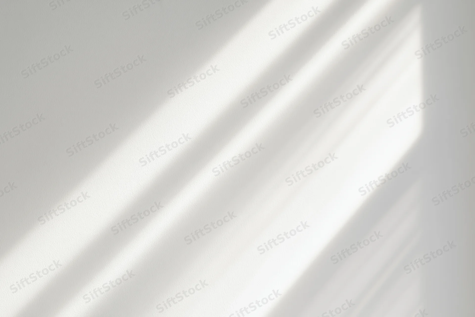 Diagonal bands of natural sunlight and soft shadow on a white interior wall