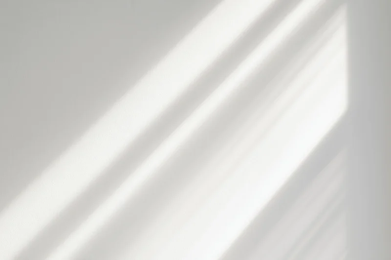 Diagonal bands of natural sunlight and soft shadow on a white interior wall