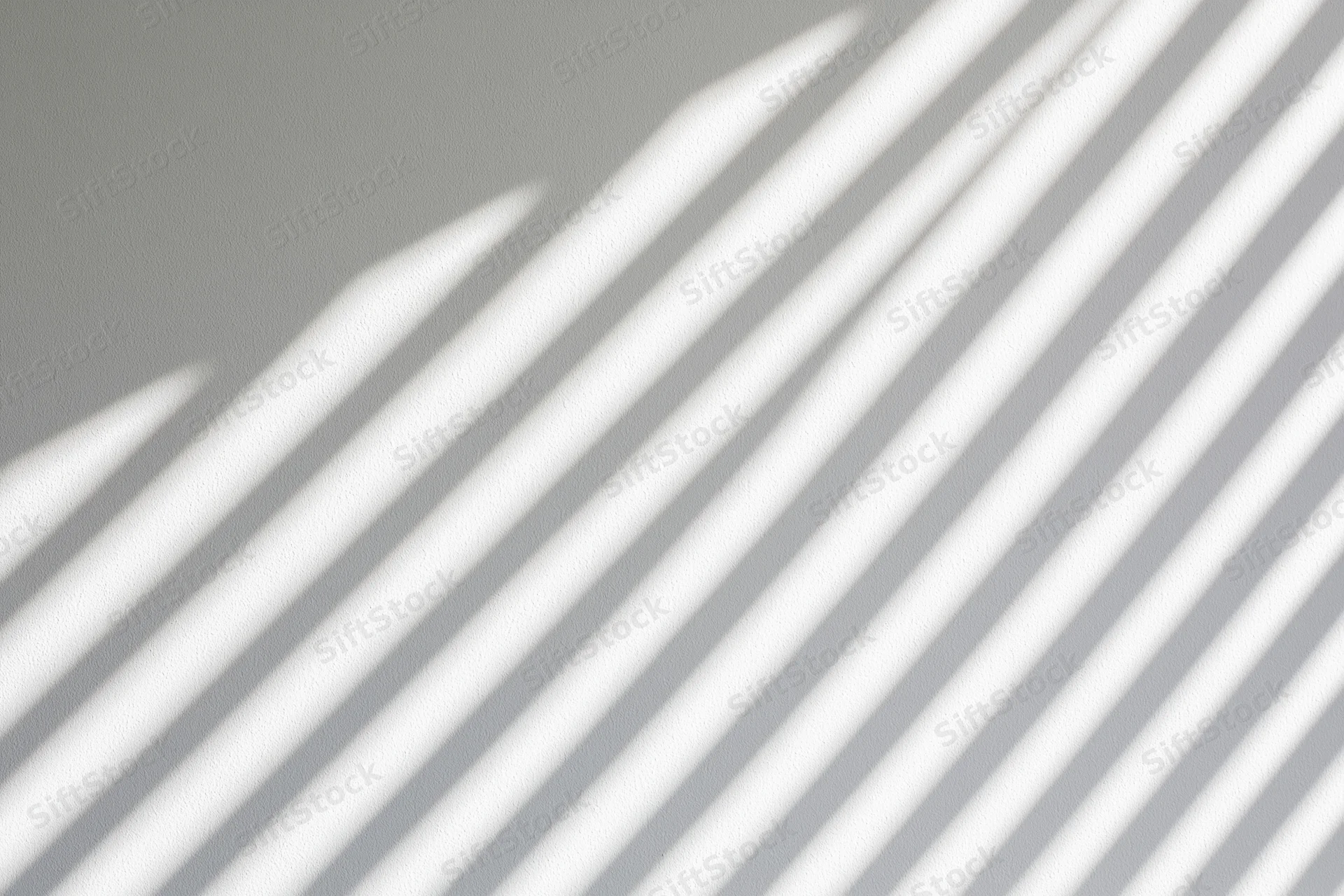 Diagonal shadow stripes from window blinds cast across a plain gray wall