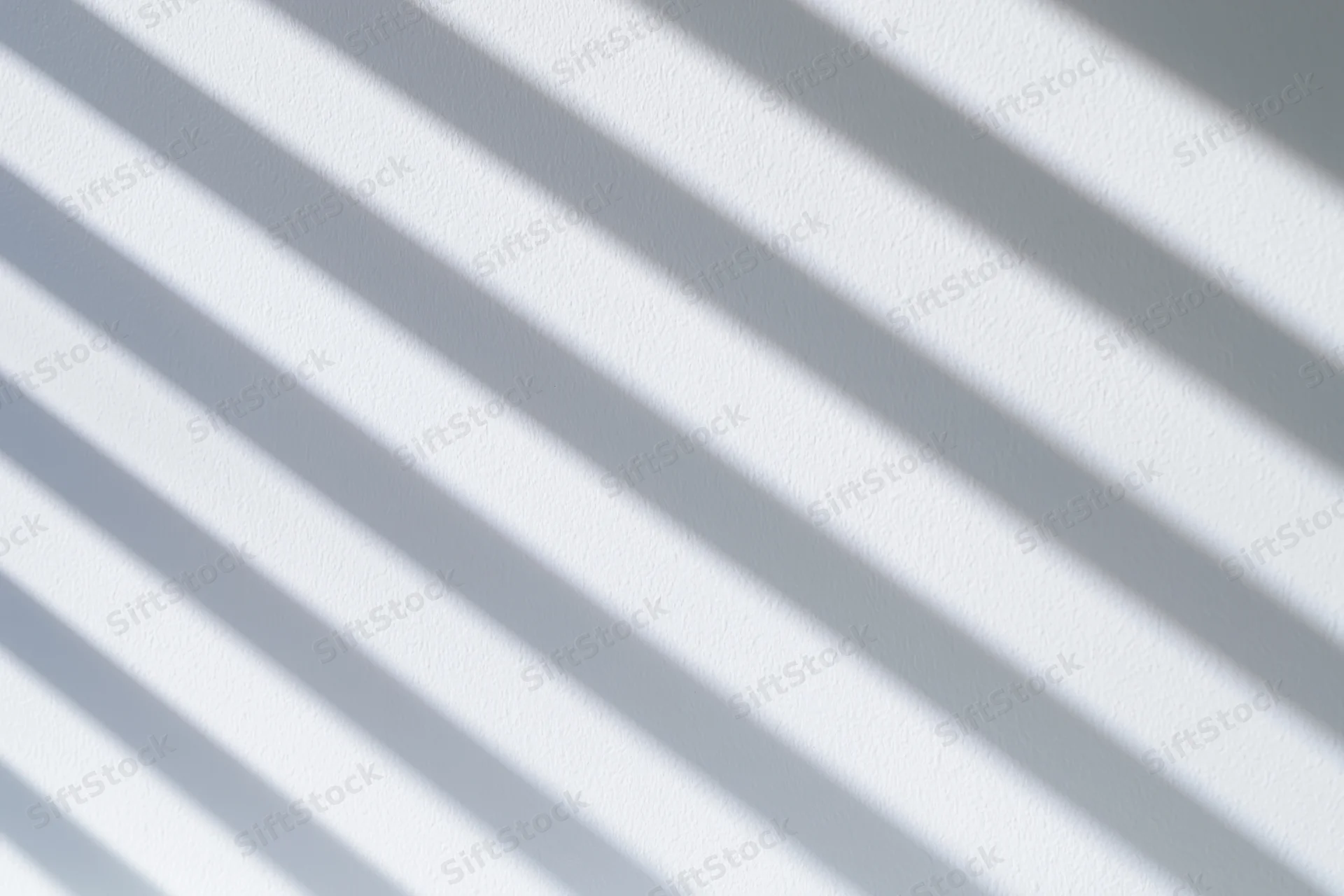 Diagonal shadow stripes from window blinds on a white wall