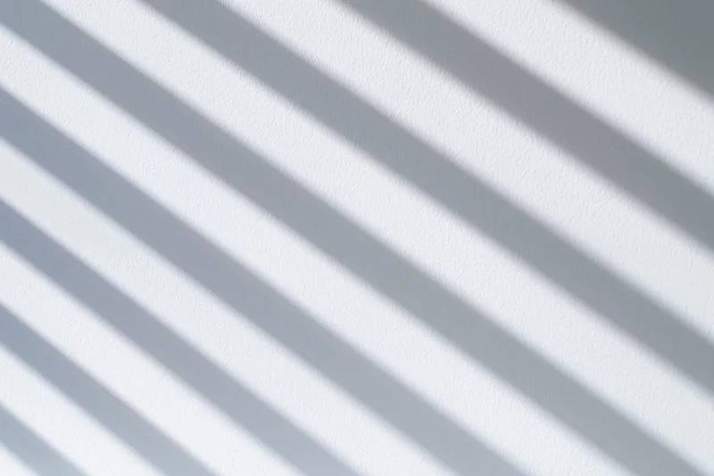 Diagonal shadow stripes from window blinds on a white wall