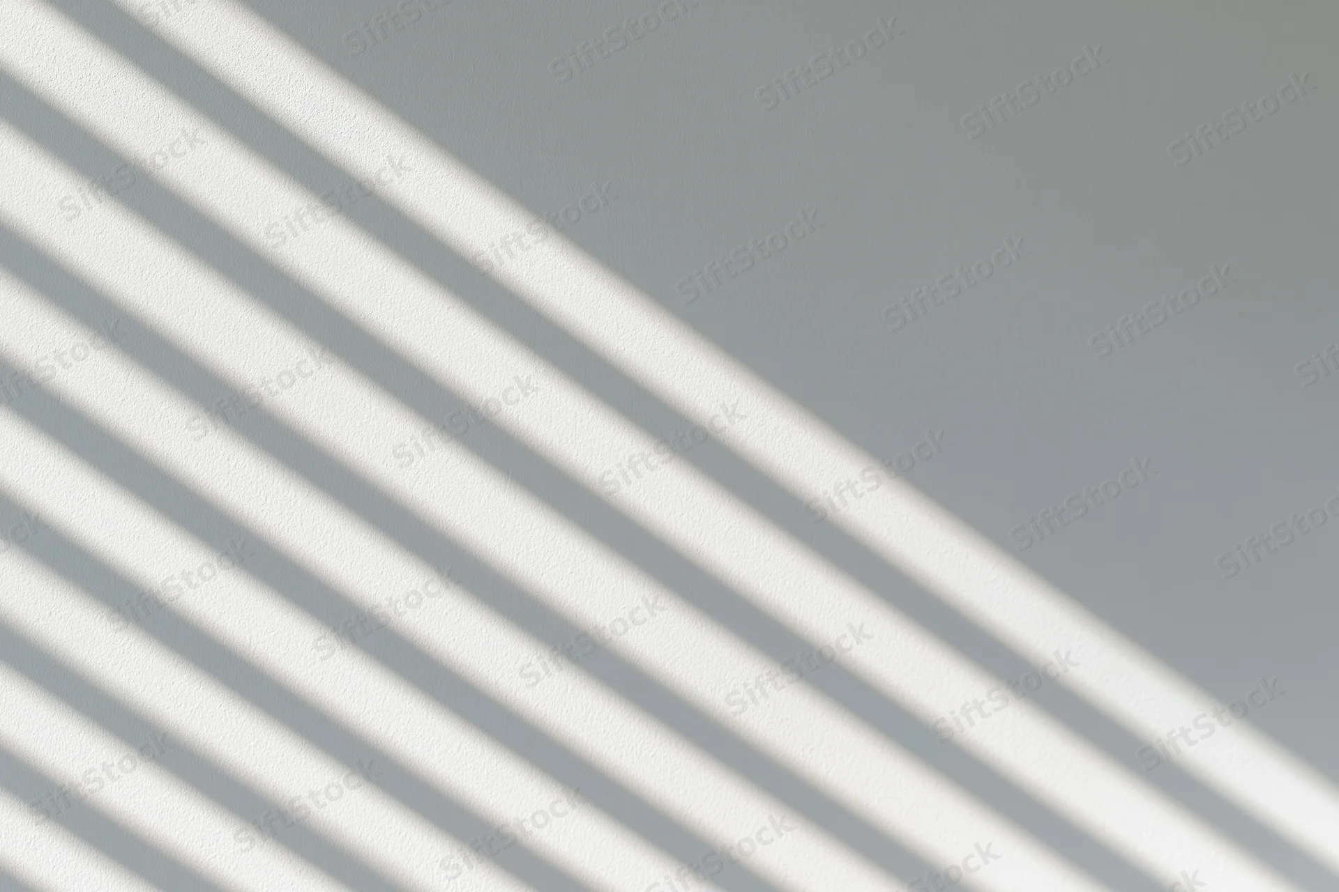 Diagonal shadow stripes from window blinds cast across a plain gray wall