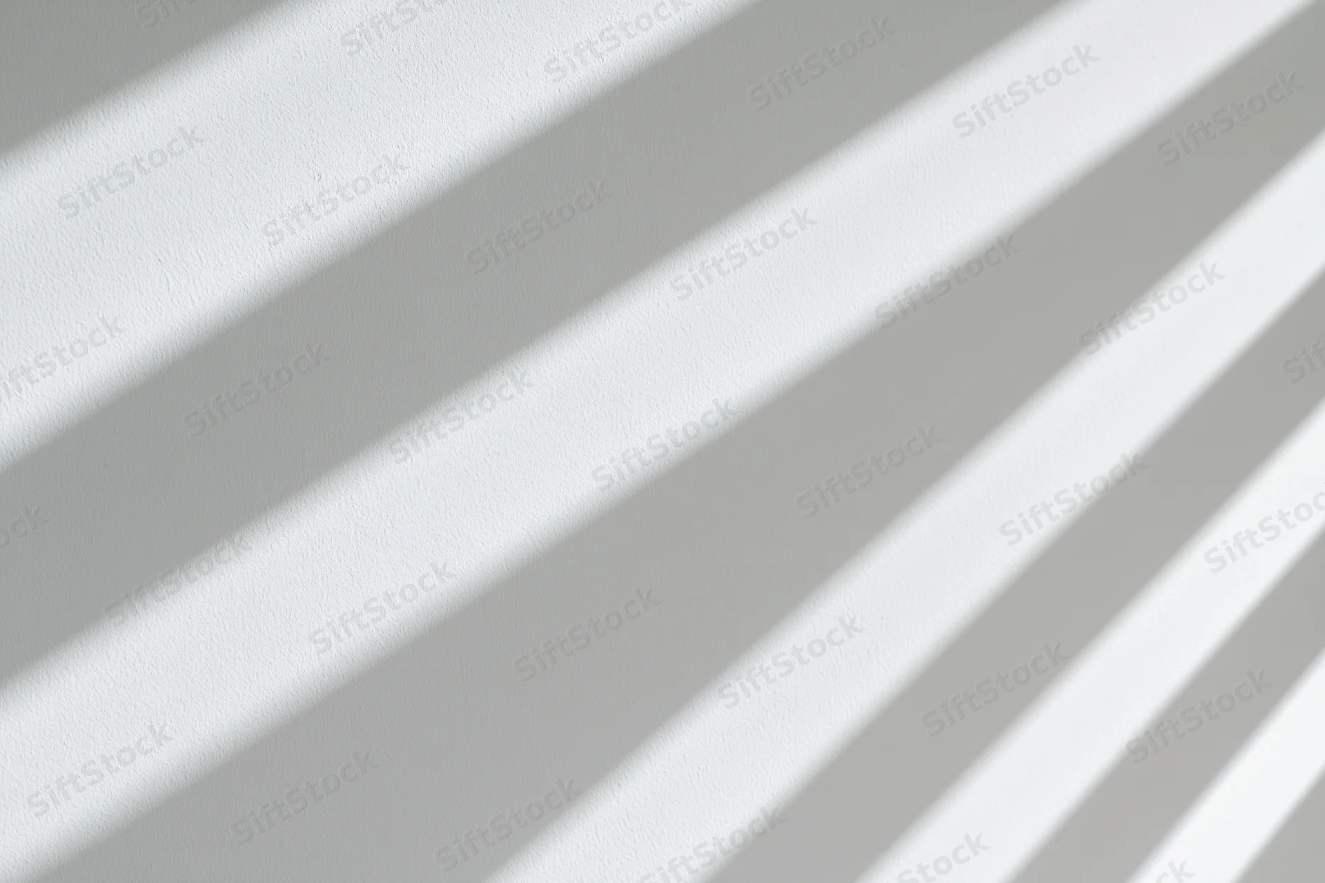 Diagonal shadow stripes from window blinds cast across a plain white wall