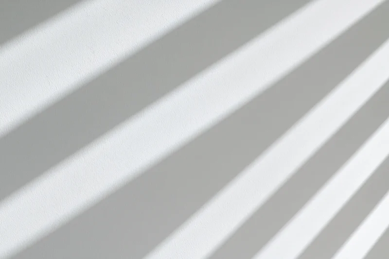 Diagonal shadow stripes from window blinds cast across a plain white wall