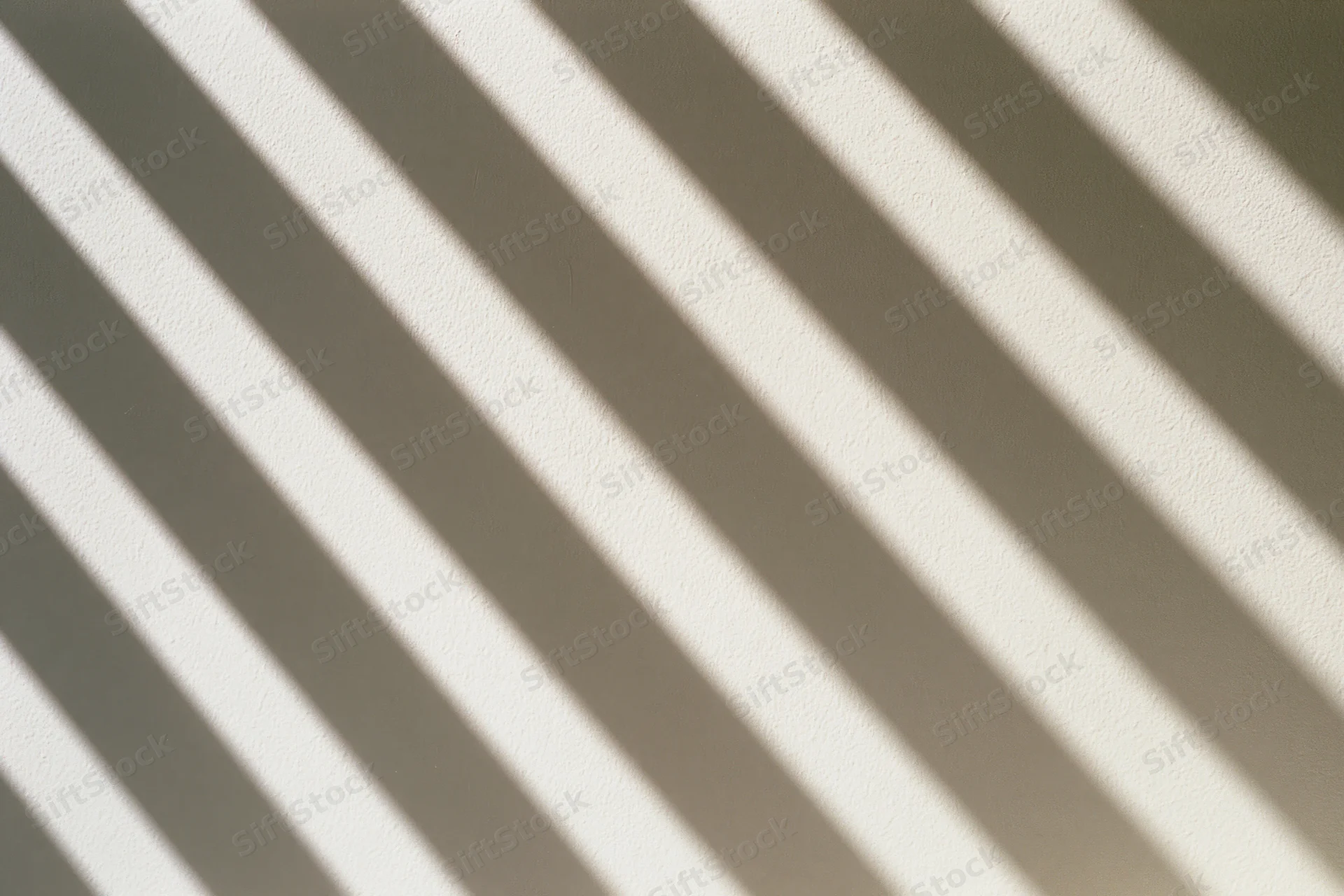 Diagonal shadows from window blinds cast across a plain white wall