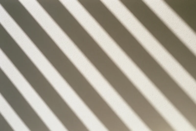 Diagonal shadows from window blinds cast across a plain white wall