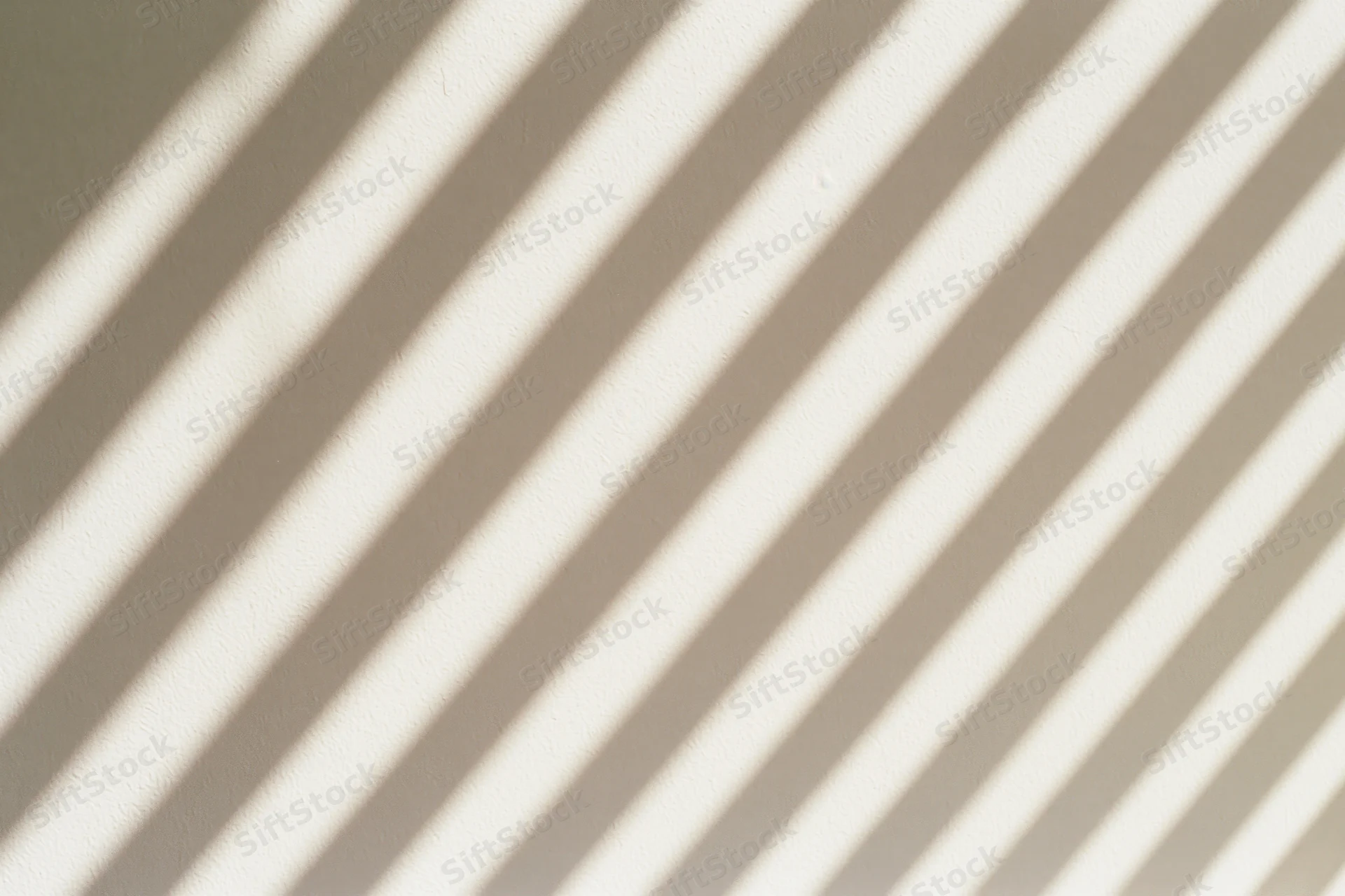 Diagonal shadows from window blinds cast across a plain white wall