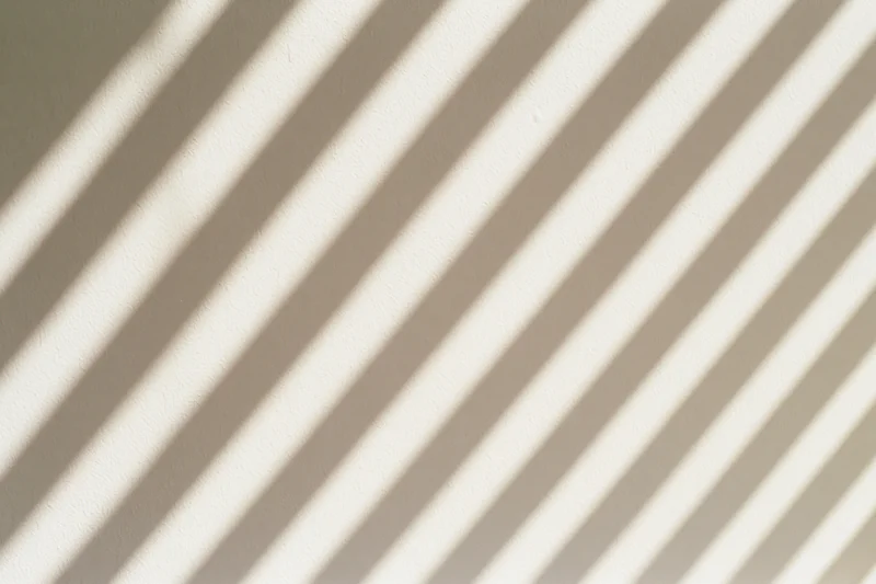 Diagonal shadows from window blinds cast across a plain white wall